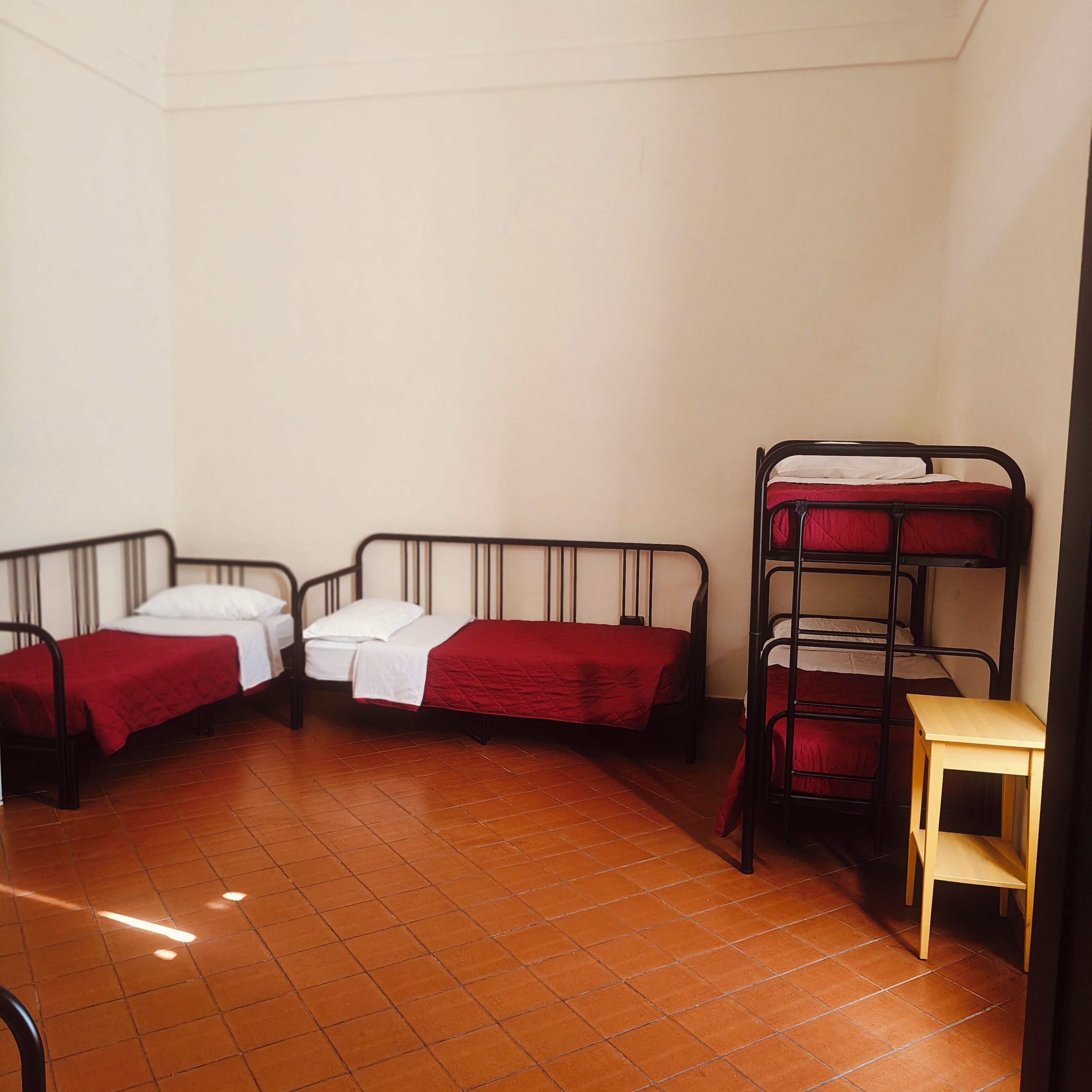 Quarto em dormitório com três camas de solteiro e uma beliche, tudo com roupa de cama vermelha.