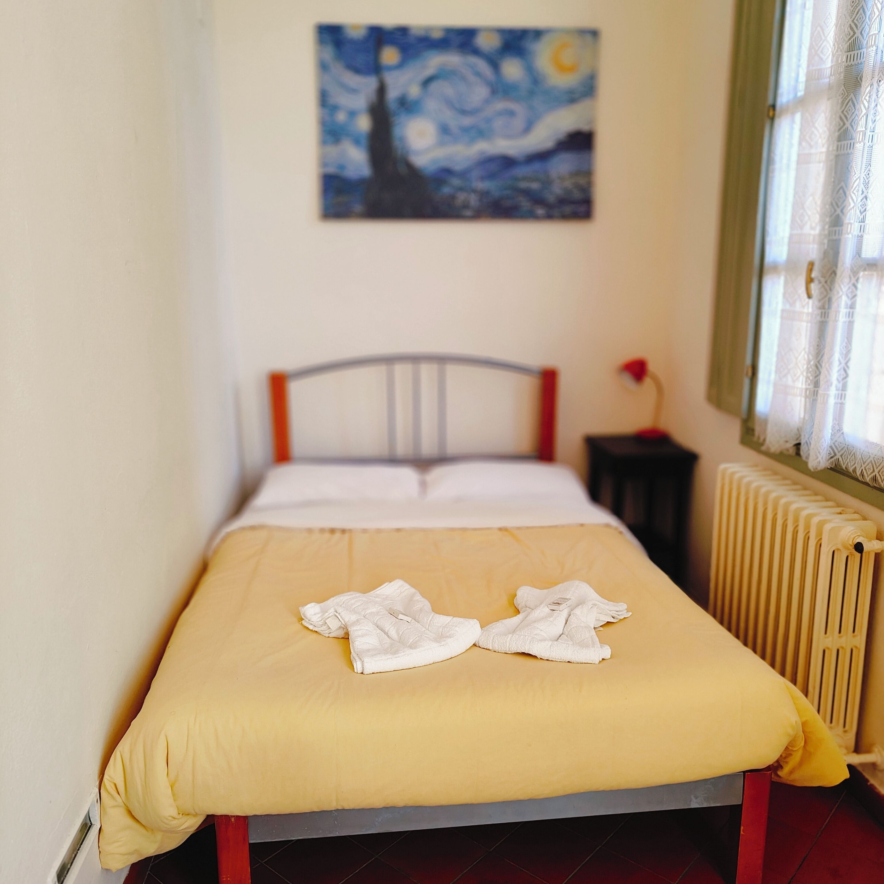 A bed with a yellow bedspread and two white towels on it. There is a painting on the wall above the bed.