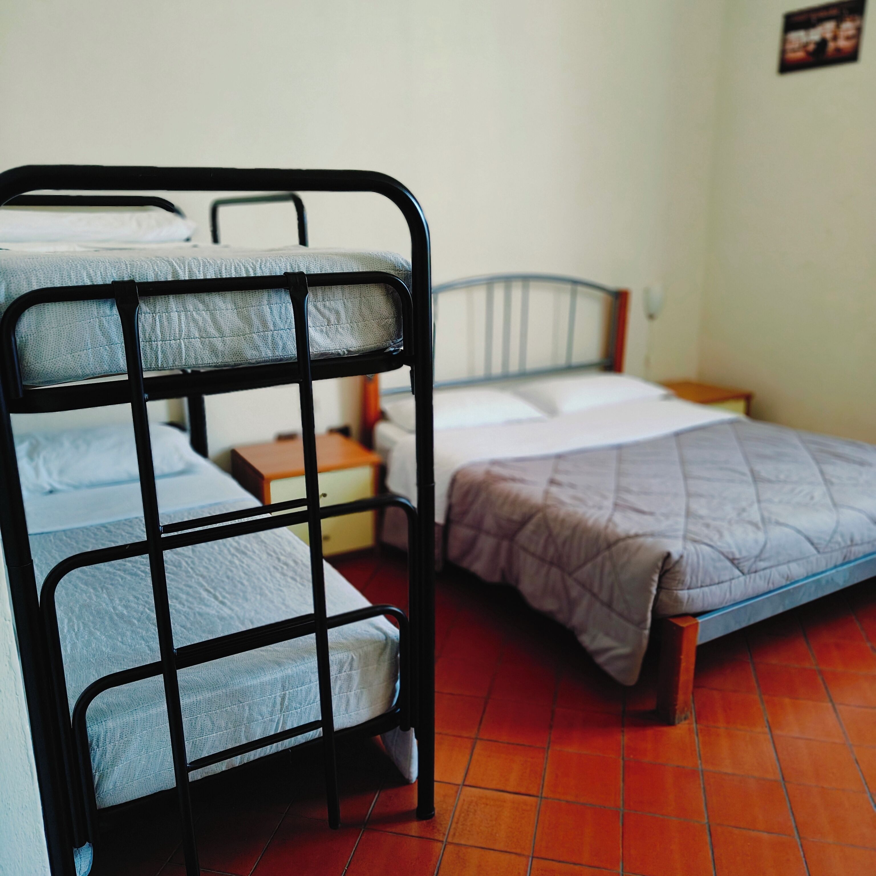 Una camera del dormitorio con letti a castello, un letto singolo, un comodino e un punto luce fissato al muro.