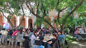 An outdoor gathering with people seated at tables under trees, in a courtyard with arches and a building in the background. - Student's Hostel della Ghiara (Reggio nell'Emilia)