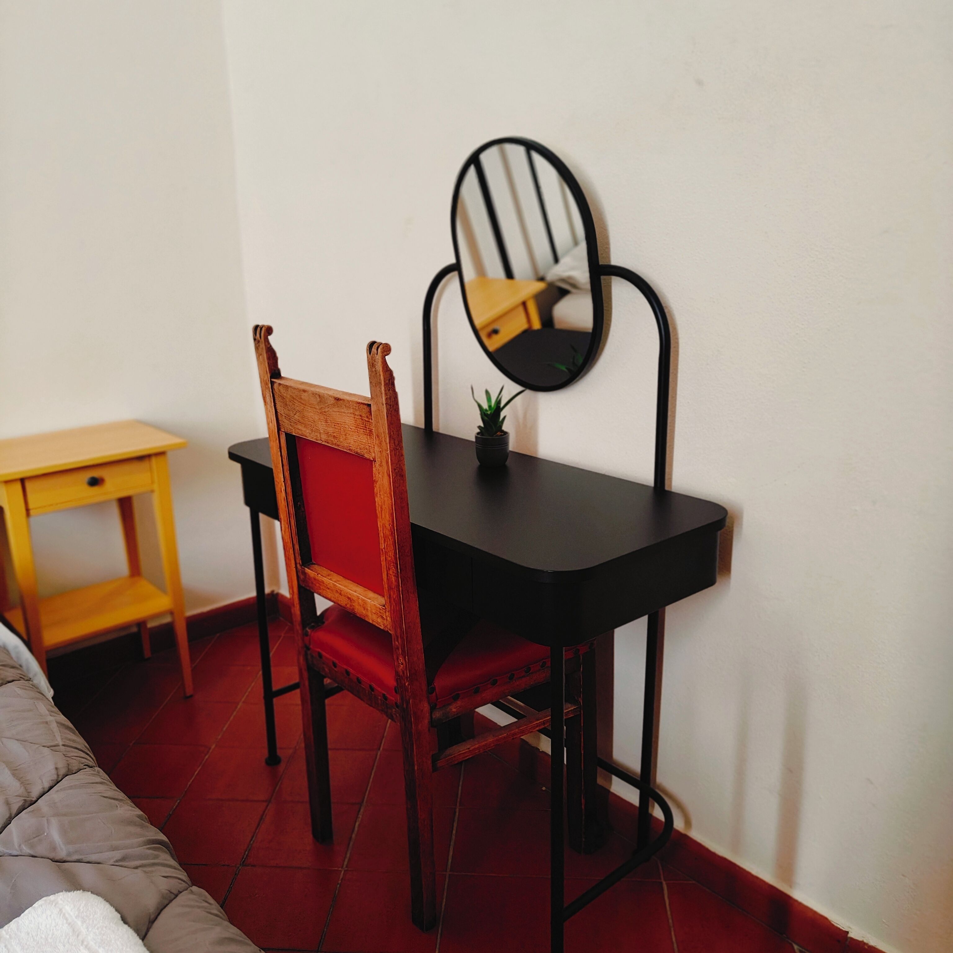 Una habitación pequeña con una silla de madera, una mesa negra y un espejo en la pared.