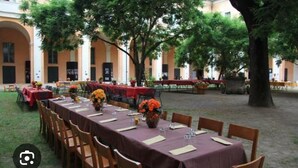 An outdoor dining area with tables set for a meal, surrounded by trees and a building with arches. - Student's Hostel della Ghiara (Reggio nell'Emilia)