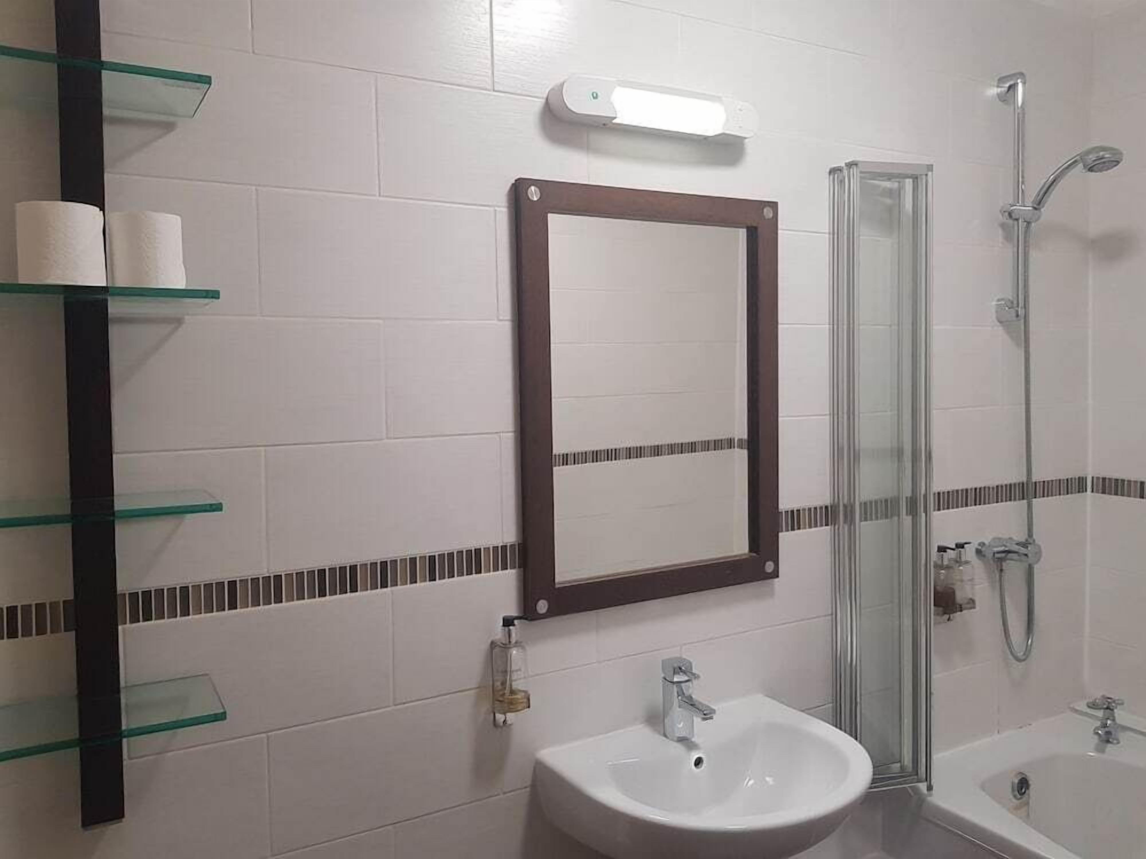 A bathroom with a glass shower enclosure, a white sink, and a mirror above it.