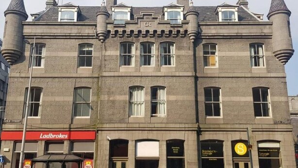 A historic building with a prominent tower, multiple windows, and a ground-level entrance with signage for Ladbrokes and Soprano's Lounge. - Soprano Hostel (Aberdeen)