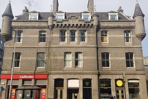 A historic building with a prominent tower, multiple windows, and a ground-level entrance with signage for Ladbrokes and Soprano's Lounge. - Soprano Hostel (Aberdeen)