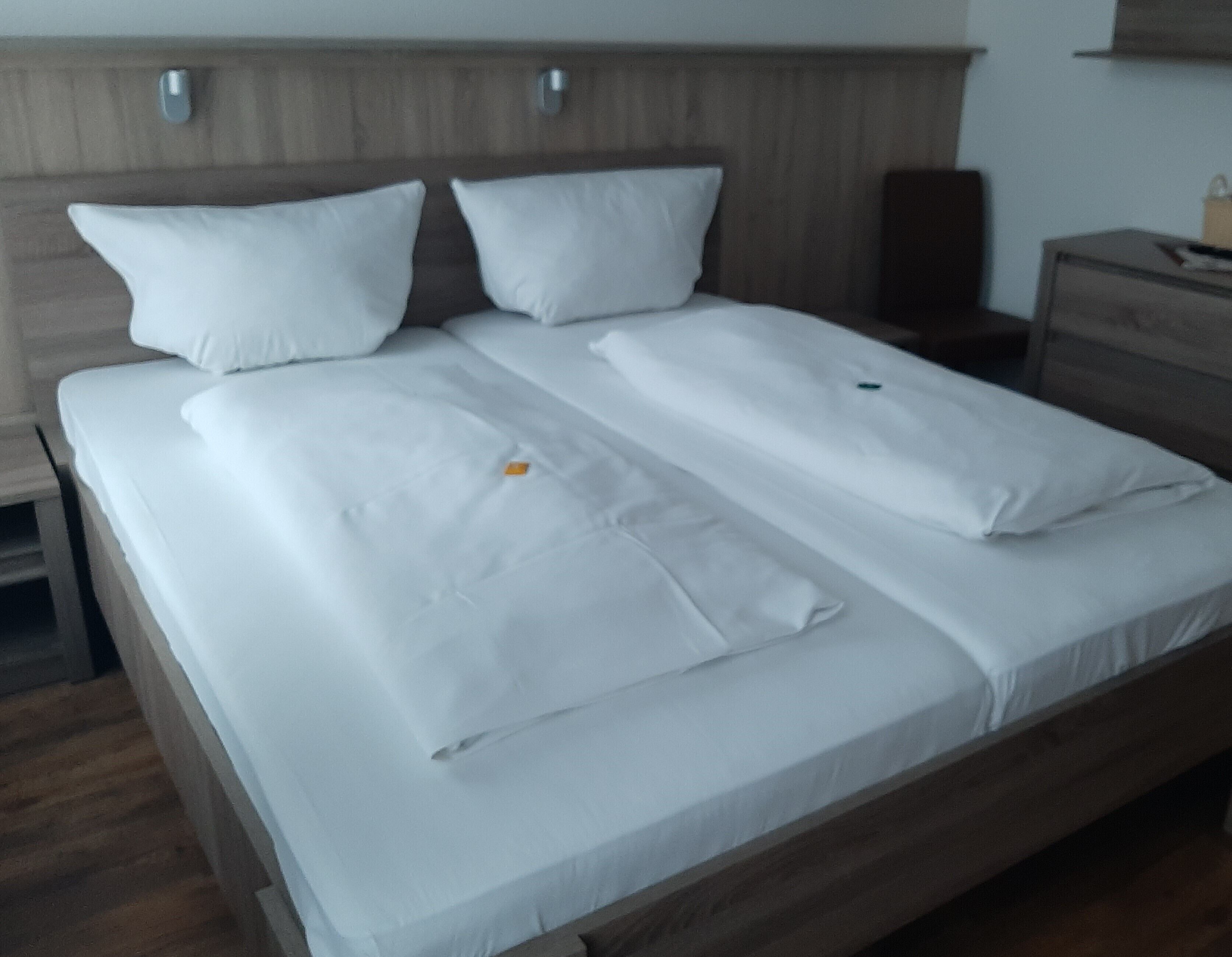 Ein ordentlich bezogenes Bett mit weißen Leinen und Kissen, ein Holzkopfschild und ein Nachttisch mit einer Lampe.