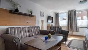 A modern living room with a sofa, armchairs, a coffee table, and a TV.