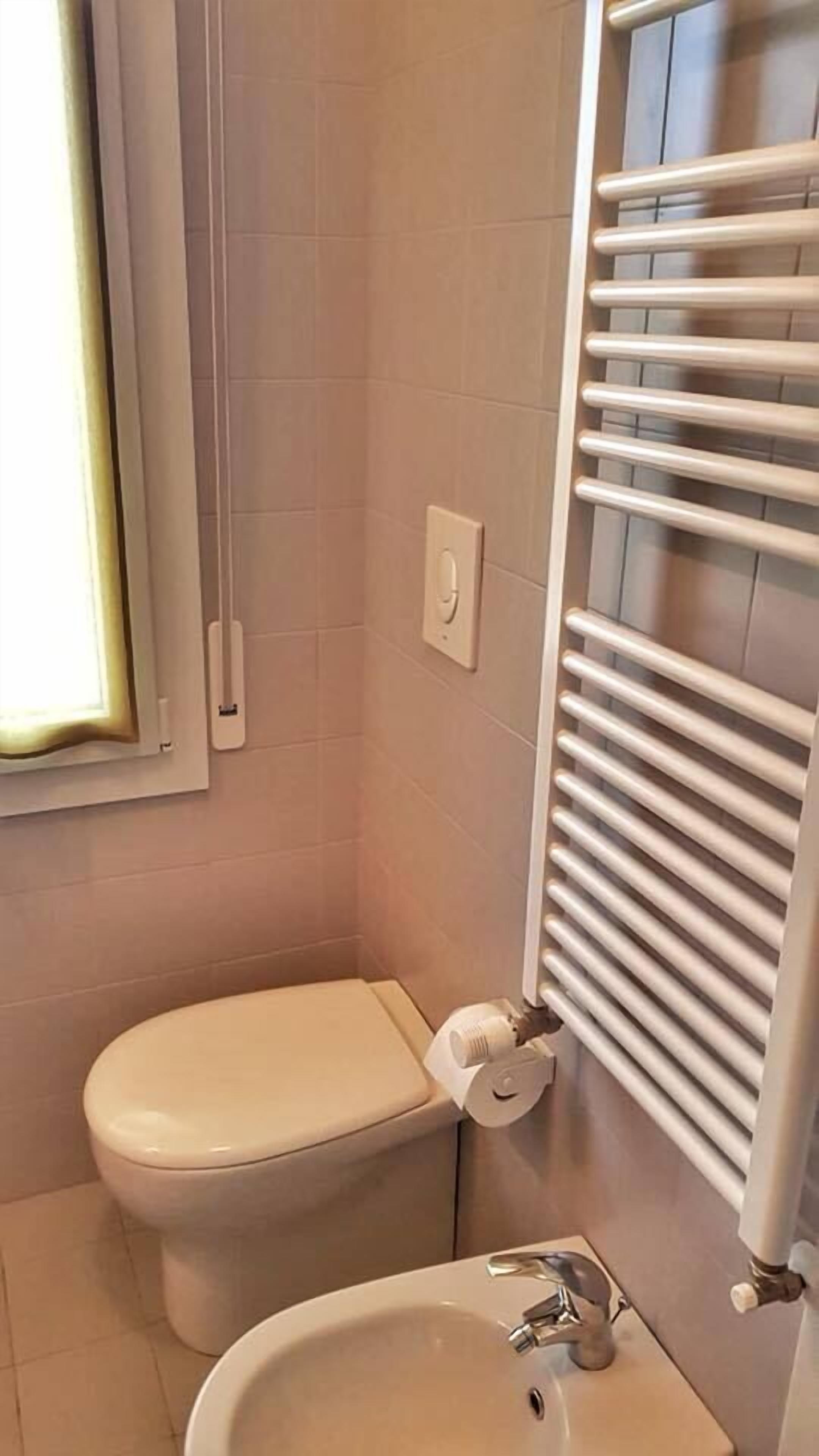 Ein Badezimmer mit Toilette, Waschbecken, Handtuchhalter und einem Fenster.