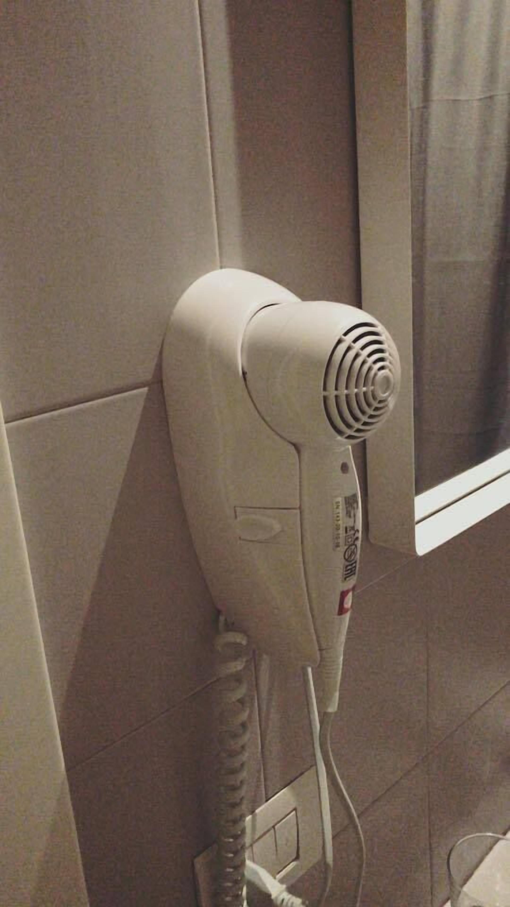 Un asciugacapelli fissato a una parete piastrellata, collegato a una presa di corrente.