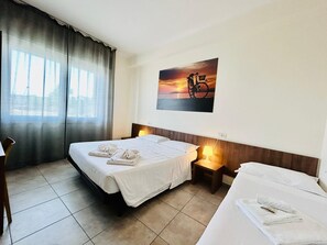 A hotel room with a bed, a bedside table with a lamp, a chair, and a window with curtains. - Hotel Bed & Bike (Cesena)