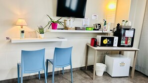 Habitación de hotel con televisor, cafetera, refrigerador pequeño, lavamanos y dos sillas azules.