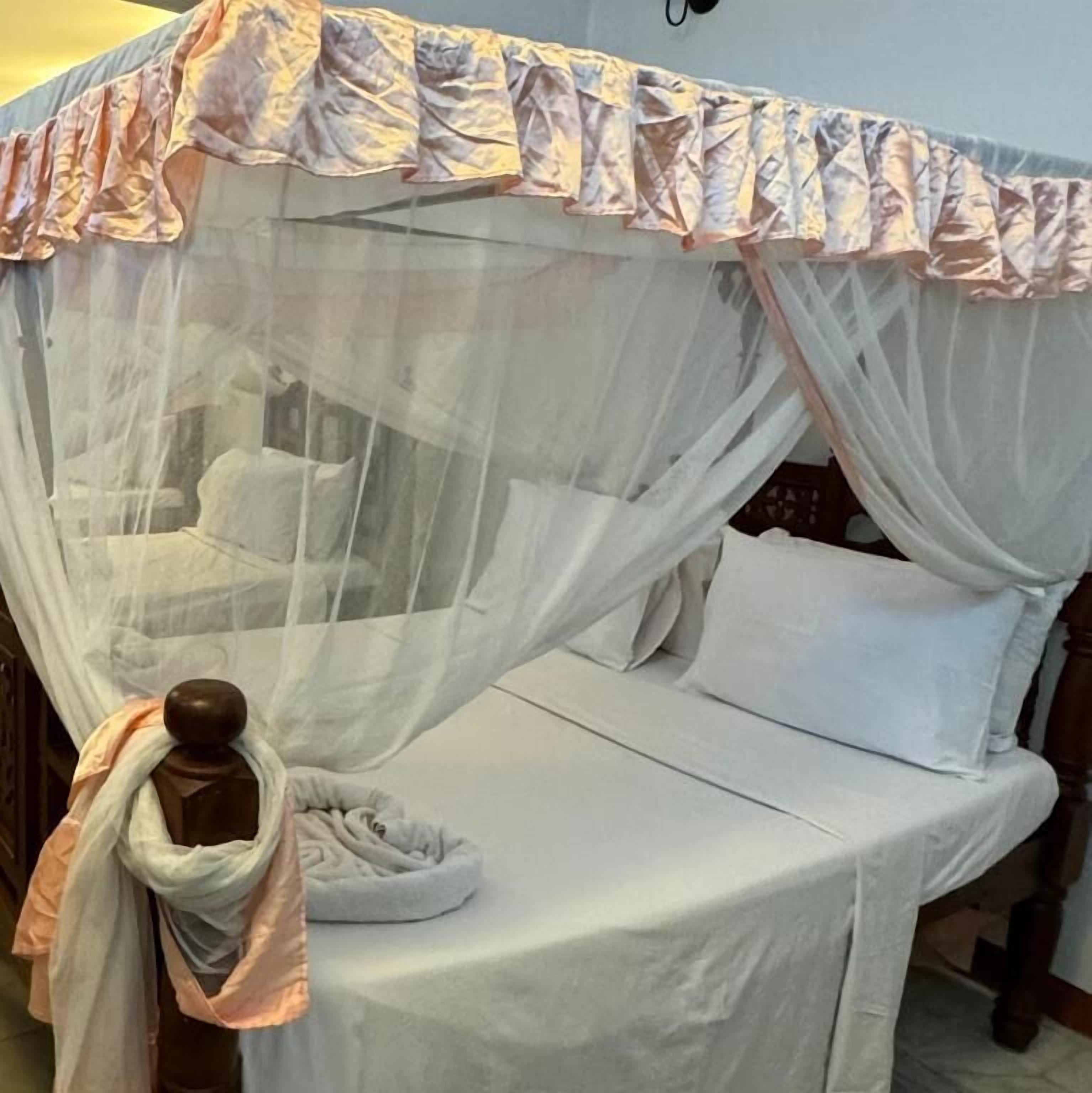 Una cama con sábana blanca y dosel con borde festoneado.