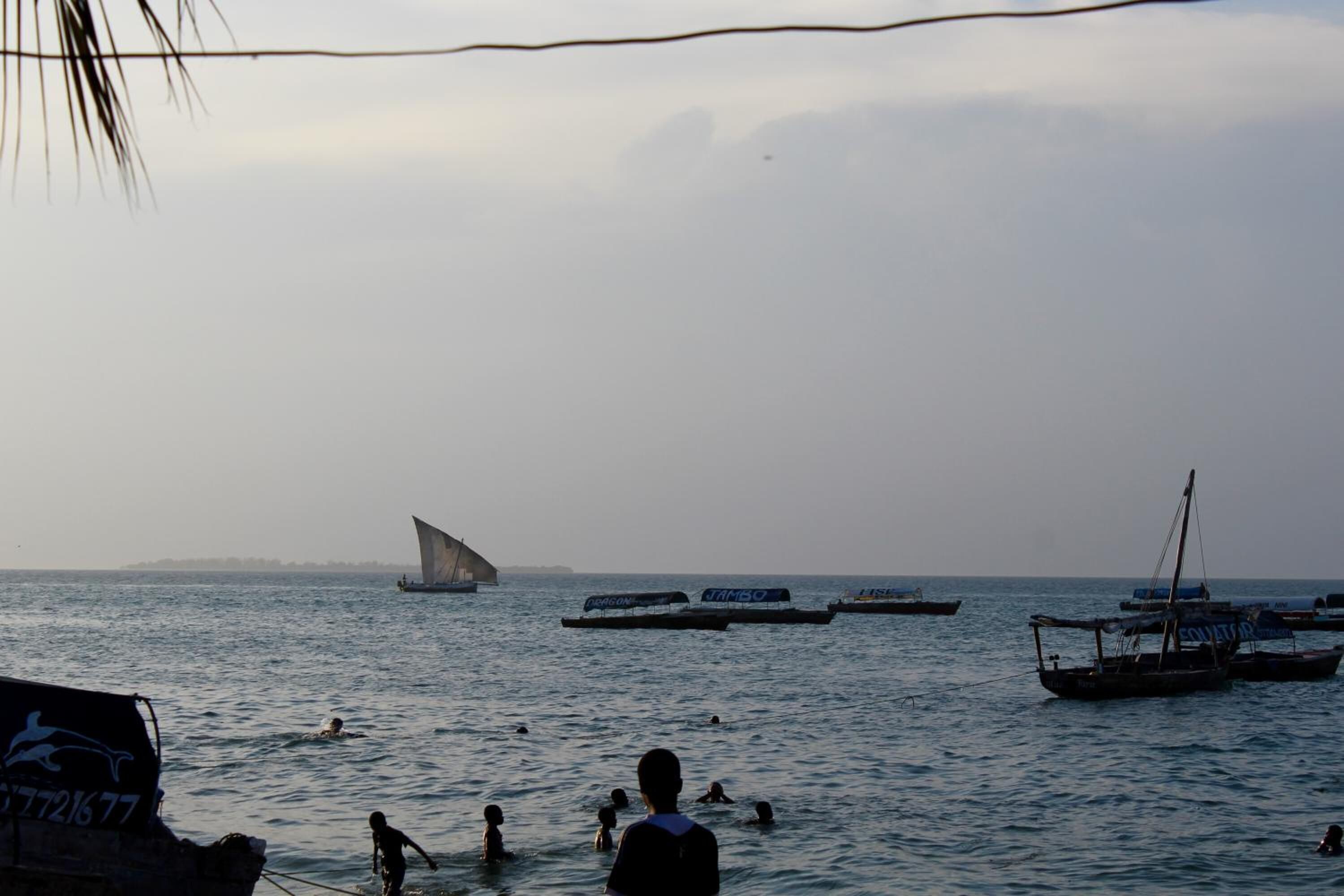 A coastal scene with boats and people swimming in the water.