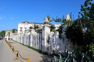 Una calle con un muro blanco y una cerca de malla metálica.