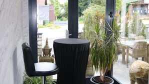 Quarto moderno com porta de vidro, uma cadeira preta, planta em vaso e área de jantar com mobiliário de vime.