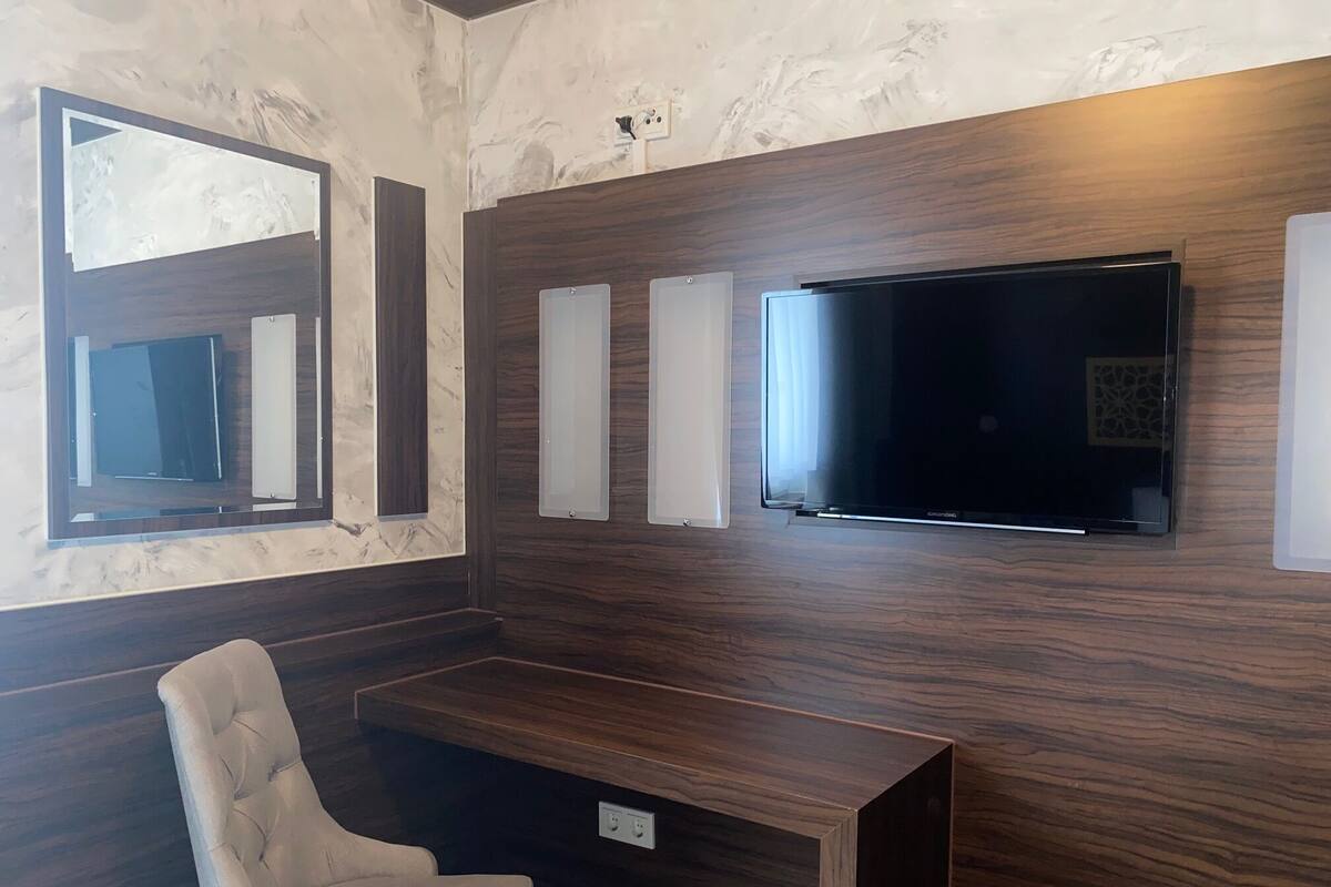 A modern room with a wooden wall, a large flat-screen TV, a cushioned chair, and a small table.