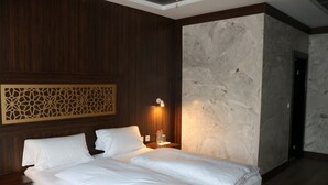 Quarto de hotel com duas camas, painéis de madeira, parede de mármore e mesa de cabeceira com abajur.