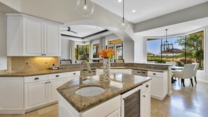 A spacious kitchen with white cabinetry, granite countertops, and a large island with a sink. - Stunning PGA  Home with Privacy and Lake Views on Golf Course (La Quinta)