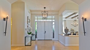 A spacious hallway with a chandelier, white doors, and a console table with decorative items. - Stunning PGA  Home with Privacy and Lake Views on Golf Course (La Quinta)
