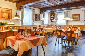 A restaurant with multiple tables and chairs, wooden beams on the ceiling, and hanging lamps. - Hotel Gasthof Rotes Rovu (Heroldsberg)