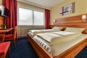 A hotel room with a bed, a desk, a chair, a television, and a window with curtains. - Hotel Gasthof Rotes Rovu (Heroldsberg)