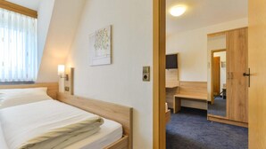 A hotel room with a bed, bedside lamps, a flat-screen TV, a wooden wardrobe, and a mirror.