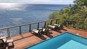 A wooden deck with a pool and lounge chairs overlooking the ocean.