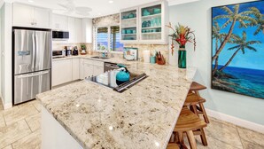 A modern kitchen with a large marble island, stainless steel appliances, and a view of the ocean through the window.