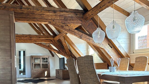 A spacious dining area with a high ceiling and exposed wooden beams, featuring wicker chairs and a central table with a glass top. - Gasthaus zum Adler (Ettenheim)