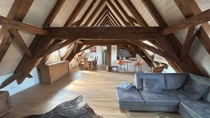 An attic space with exposed wooden beams, a dining area with a round table and chairs, a sofa, and a coffee table. - Gasthaus zum Adler (Ettenheim)