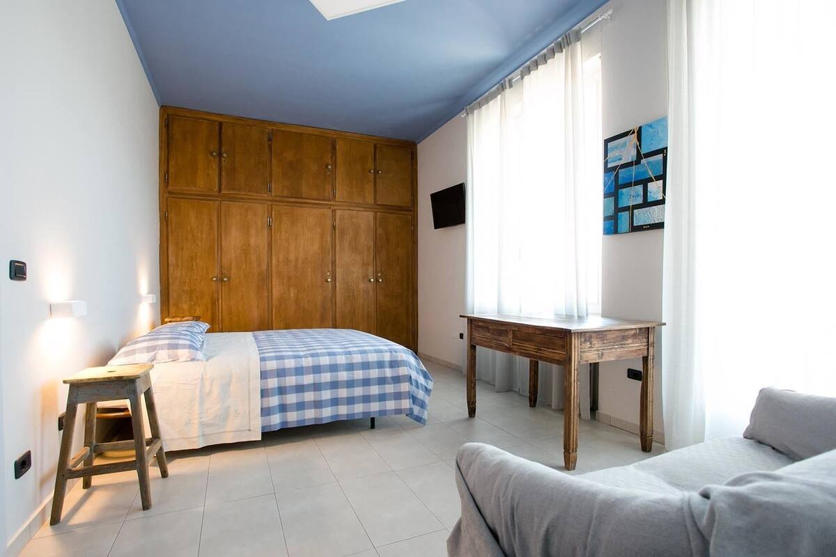 A bedroom with a bed, a wooden wardrobe, a desk, and a window with curtains.