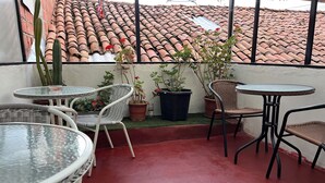 A terrace with round glass tables and wicker chairs, surrounded by potted plants and a red floor. - Casa Salkantay B&B (Cusco)