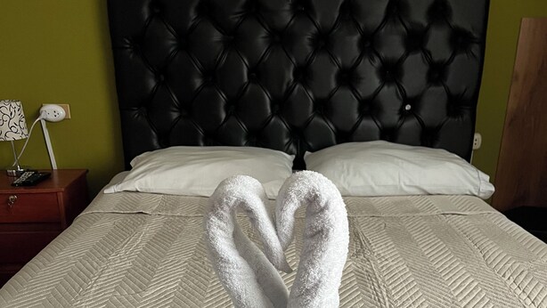 A bed with a quilted headboard and two towels arranged in a heart shape. - Casa Salkantay B&B (Cusco)