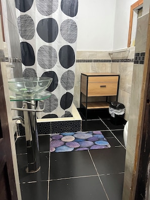 Een badkamer met een glazen wastafel, een houten kast en een behang met een patroon.