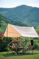 Dos personas sentadas en una mesa bajo un amplio toldo, con un paisaje montañoso al fondo.