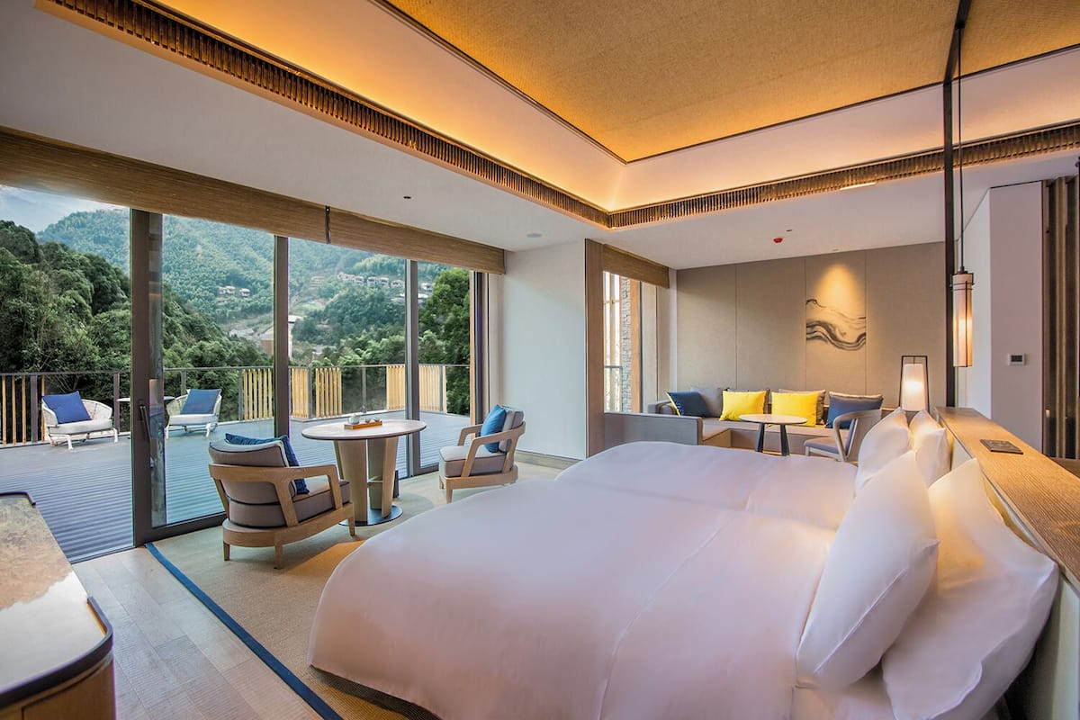 Ein geräumiges Schlafzimmer mit einem großen Bett, einem Balkon mit Sitzgelegenheit und Blick ins Freie.