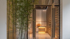 Un interior moderno con plantas de bambú, un mostrador de recepción y un panel de madera con listones.