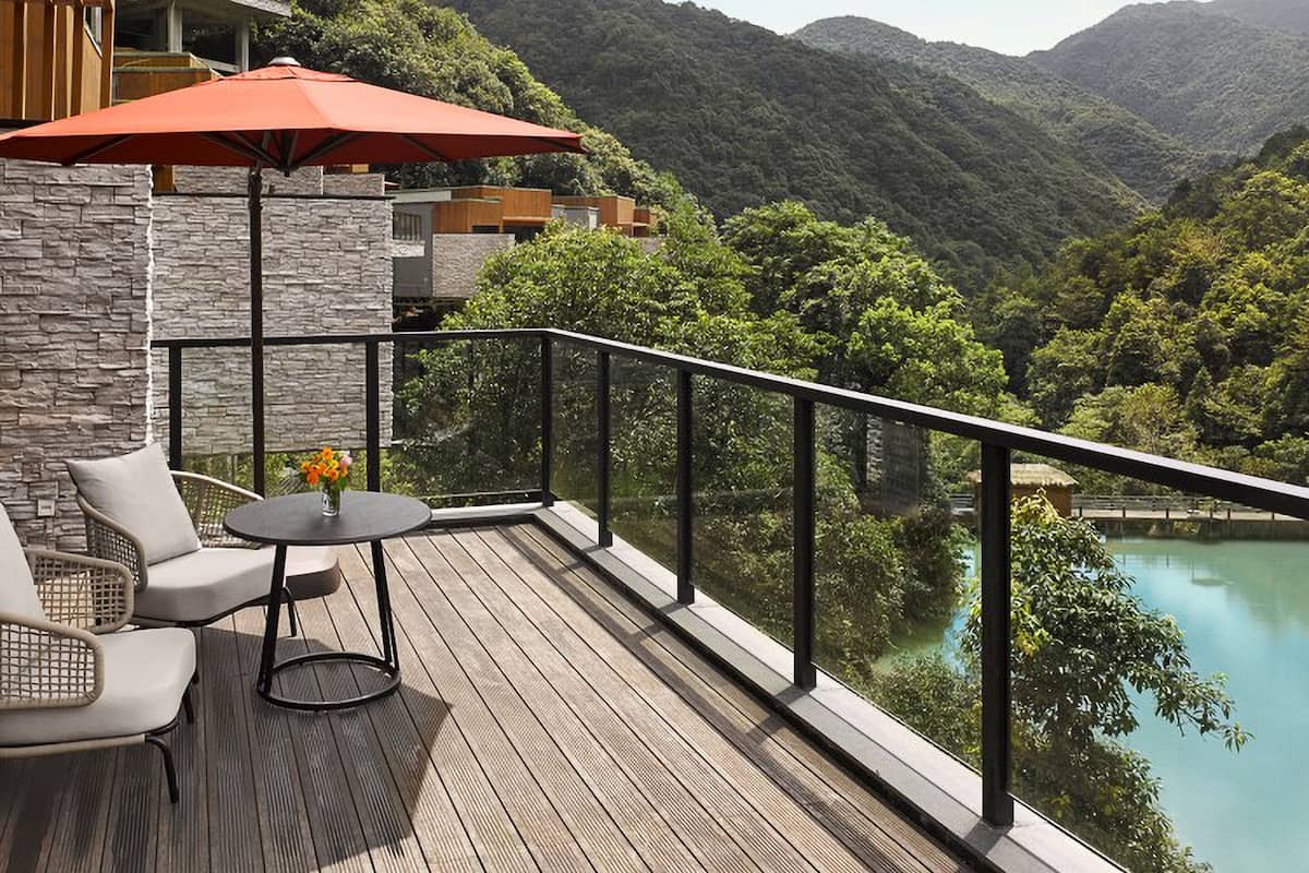 Ein Balkon mit Holzboden, einem Tisch und Stühlen sowie einem roten Sonnenschirm.