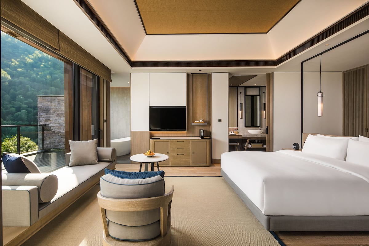 Ein modernes Hotelzimmer mit Balkon, einem Bett, einer Couch, einem runden Tisch und einem Fernseher.