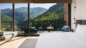 Habitación de hotel moderna con una cama grande, balcón con asientos y una vista panorámica a las montañas.
