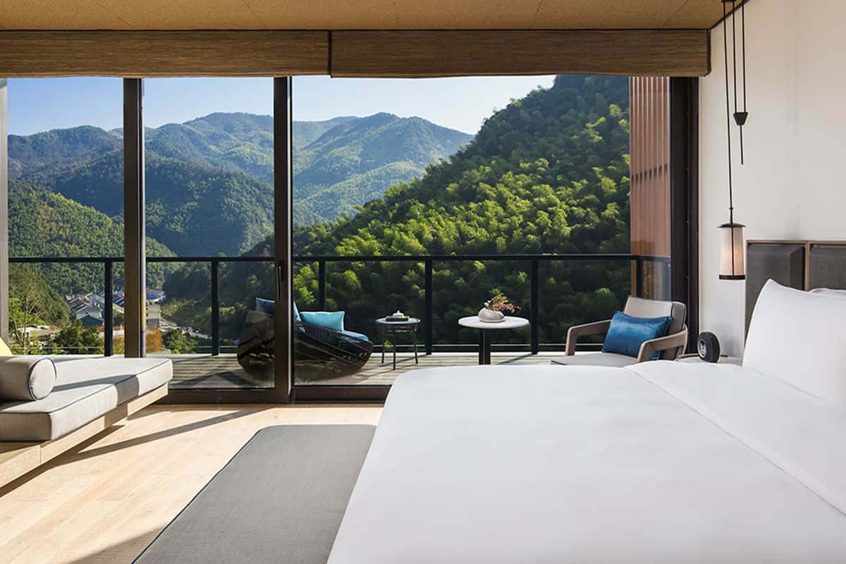 Ein modernes Hotelzimmer mit einem großen Bett, einem Balkon mit Sitzgelegenheit und einem schönen Bergblick.