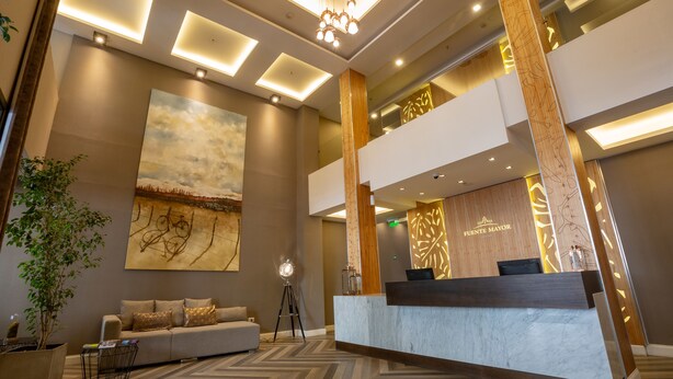 Un moderno vestíbulo de hotel con un mostrador de recepción, un sofá, un cuadro abstracto de gran tamaño y una planta en maceta.