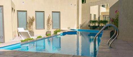 Una piscina exterior moderna con agua azul cristalina, rodeada de un diseño arquitectónico minimalista, y equipada con una escalera de metal.