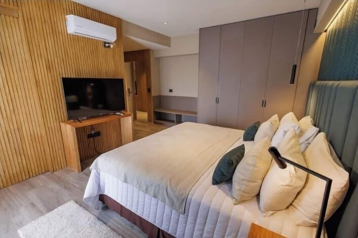 Un dormitorio moderno con una cama grande, televisor integrado, armario y una pequeña zona de estar.