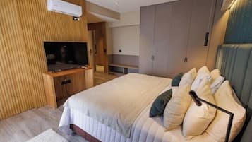 A modern bedroom with a large bed, built-in TV, wardrobe, and a small seating area.