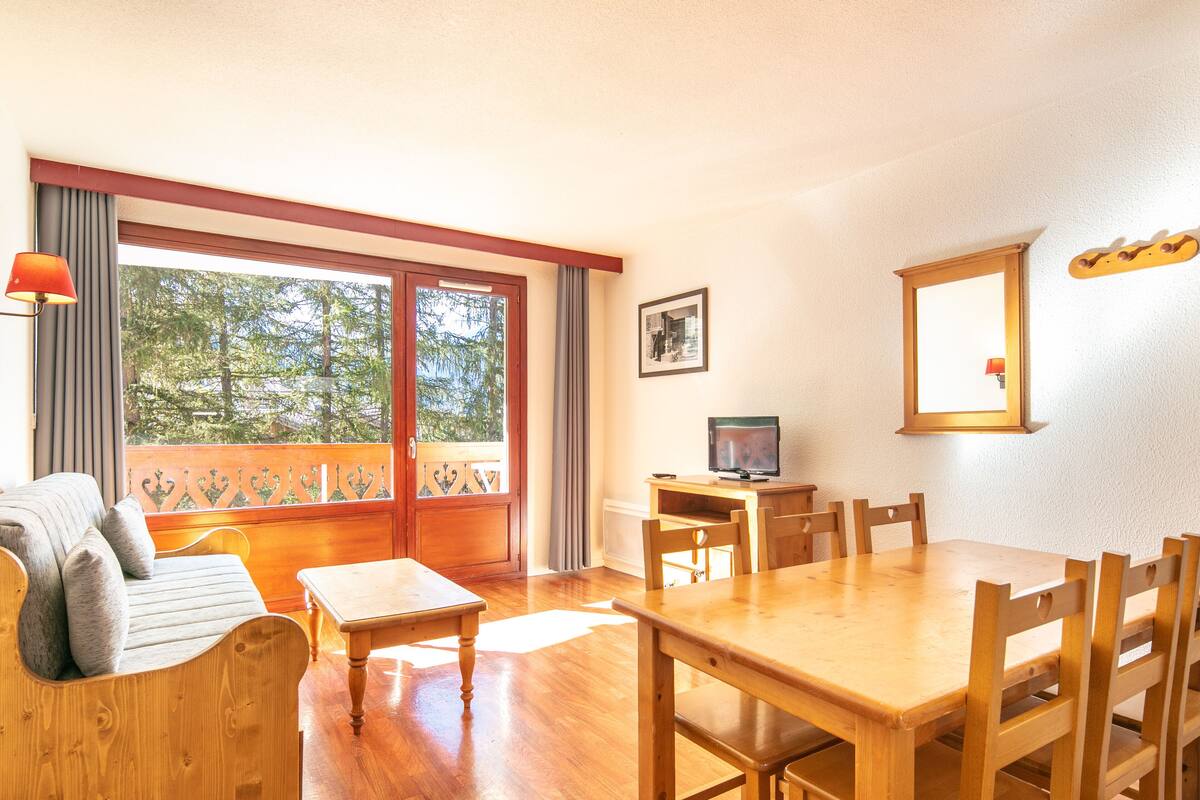 Une pièce chaleureuse avec une table à manger en bois, des chaises, un canapé et un téléviseur posé sur un meuble en bois.