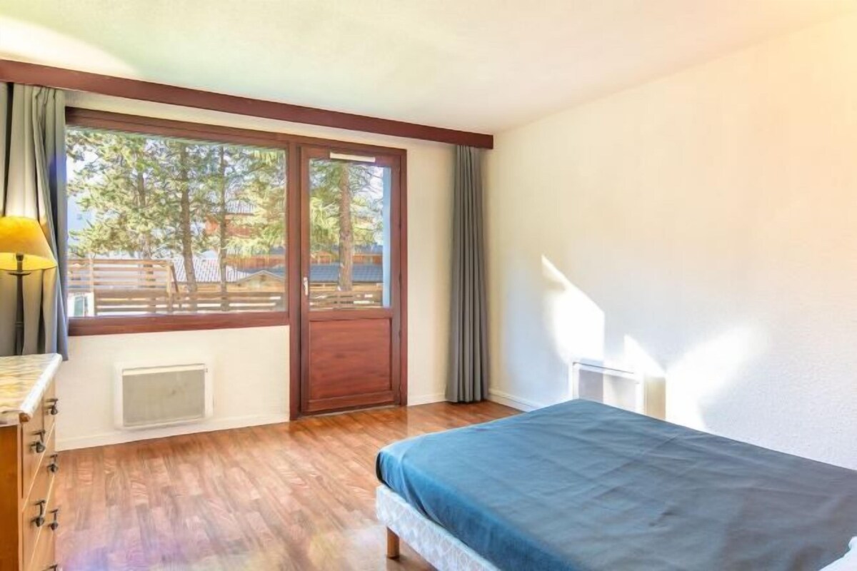 Une chambre avec une grande fenêtre, un lit, une table de chevet et une lampe.