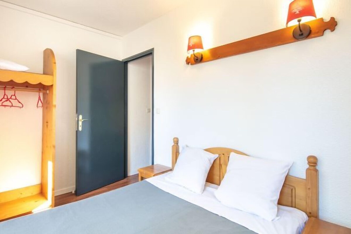 Une chambre à coucher comprenant un lit, une tête de lit en bois, des tables de chevet, une armoire et une lampe fixée au mur.