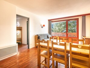 Una habitación con una mesa de madera, sillas, un sofá y una ventana con vistas a árboles.