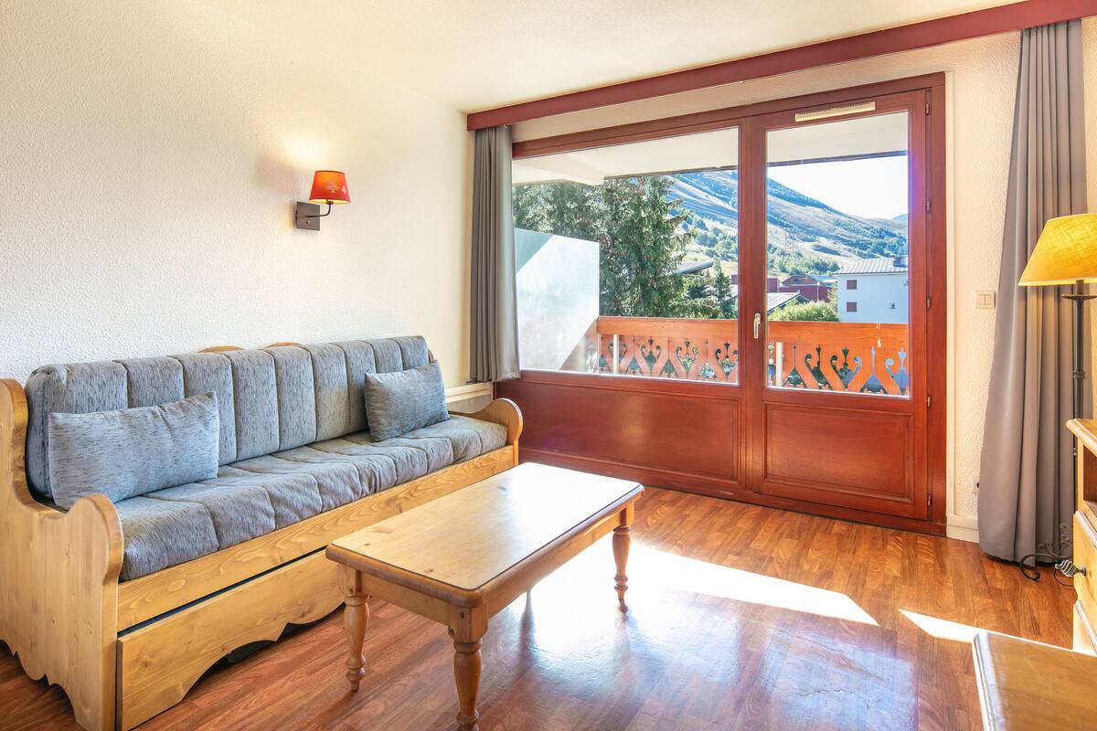 Une pièce avec un canapé en bois, une table basse en bois, une vue à travers une porte-fenêtre coulissante et une lampe sur la droite.